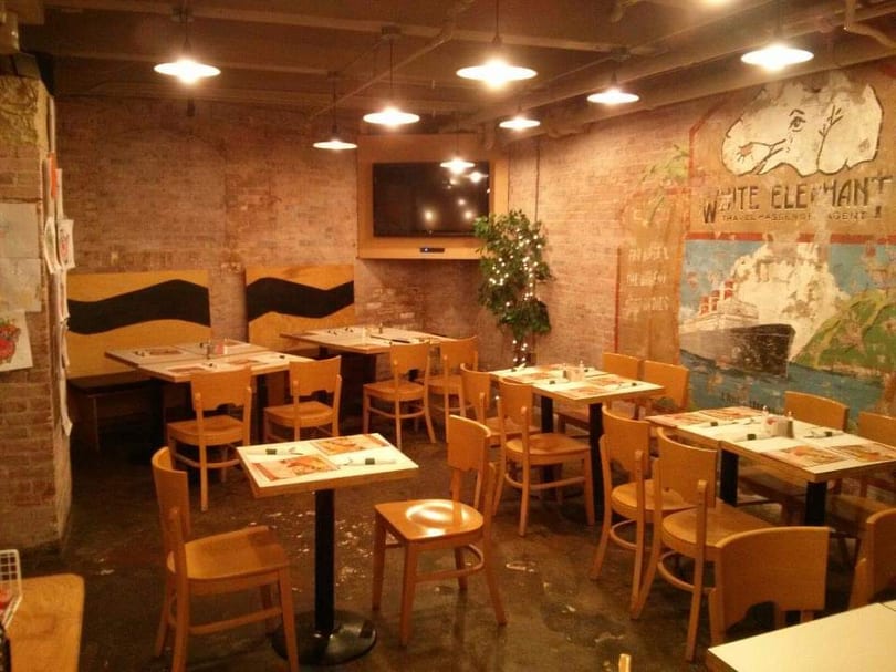 Cozy restaurant interior with exposed brick walls, wooden tables and chairs, and a large mural.