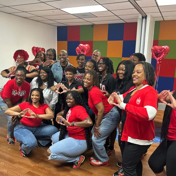 A group of women in red shirts and blue jeans posing with hand gestures and heart balloons.