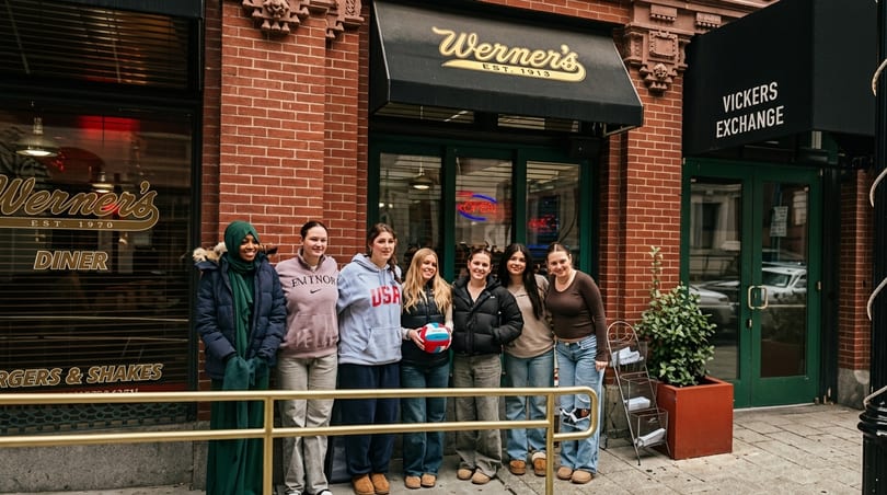 Six young women pose in front of Werner's Diner, a brick building with a black awning.