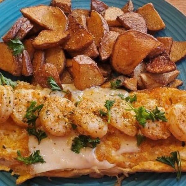 Seafood omelette with crab and shrimp, topped with parsley, served with roasted potatoes on a blue plate.