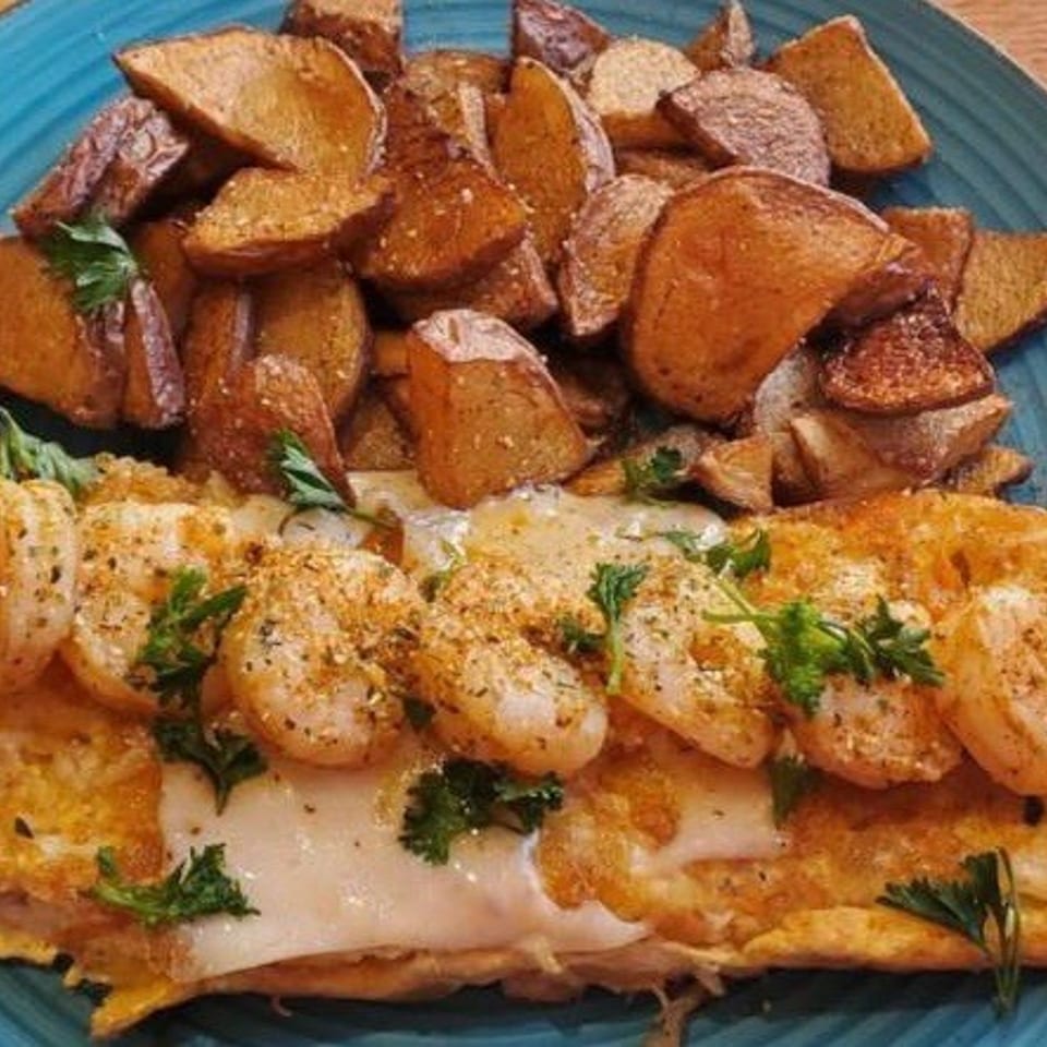 Seafood omelette with crab and shrimp, topped with parsley, served with roasted potatoes on a blue plate.