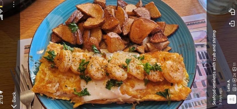 Seafood omelette with crab and shrimp, topped with parsley, served with roasted potatoes on a blue plate.