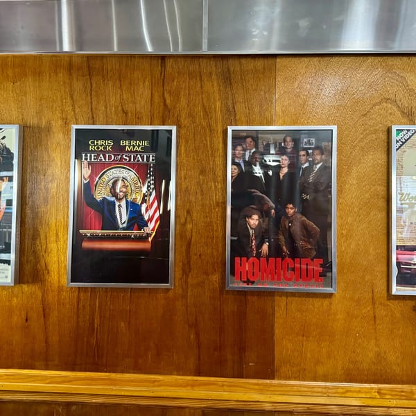 Four framed movie posters, including "Syriana" and "Head of State," hang on a wooden wall.
