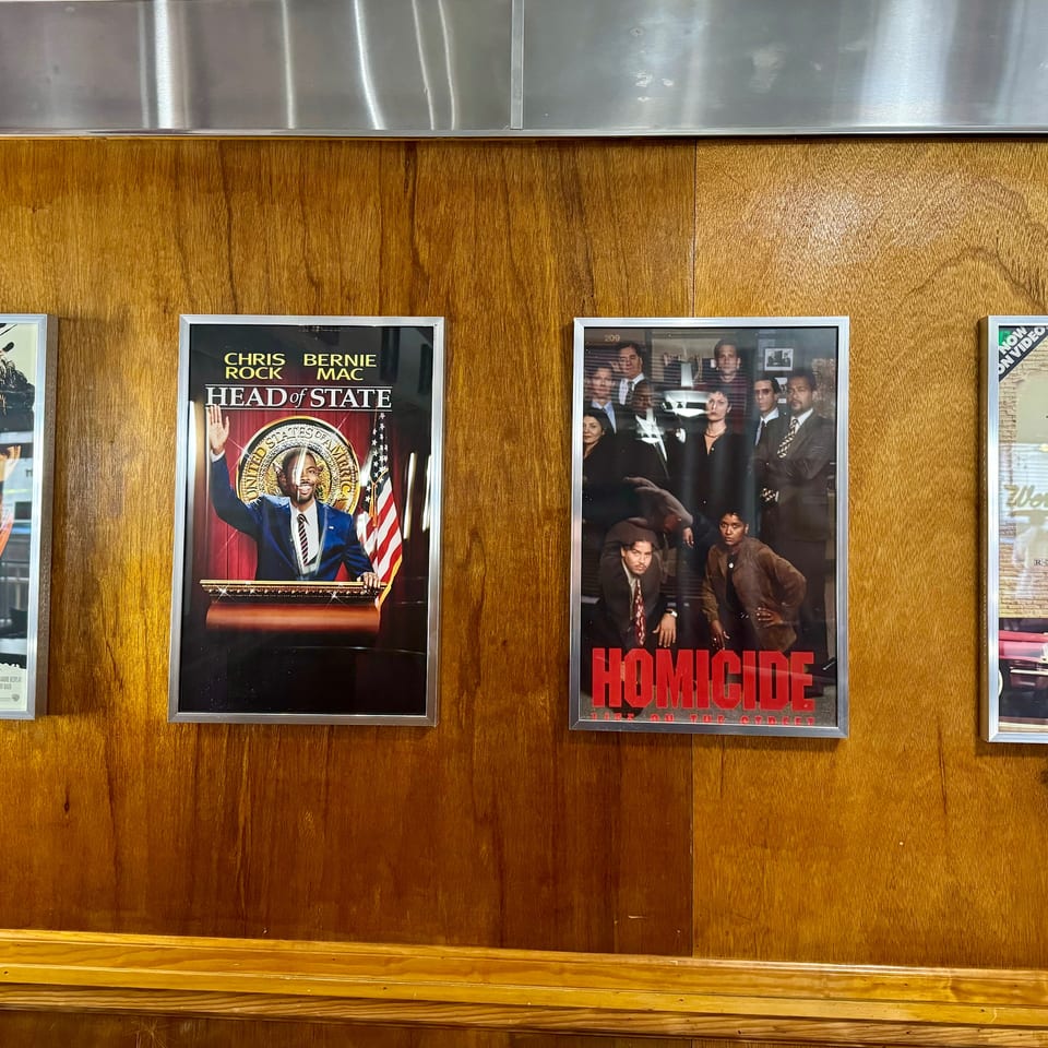 Four framed movie posters, including "Syriana" and "Head of State," hang on a wooden wall.