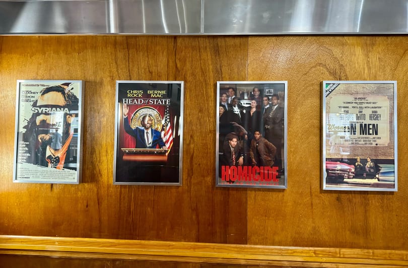 Four framed movie posters, including "Syriana" and "Head of State," hang on a wooden wall.