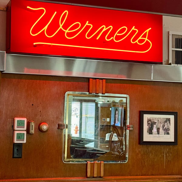 Red neon sign for "Werners" above a wooden wall with a mirror and framed picture.