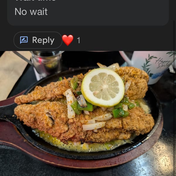 Crispy fried fish fillets topped with sliced lemon, onions, and green peppers in a sizzling skillet.