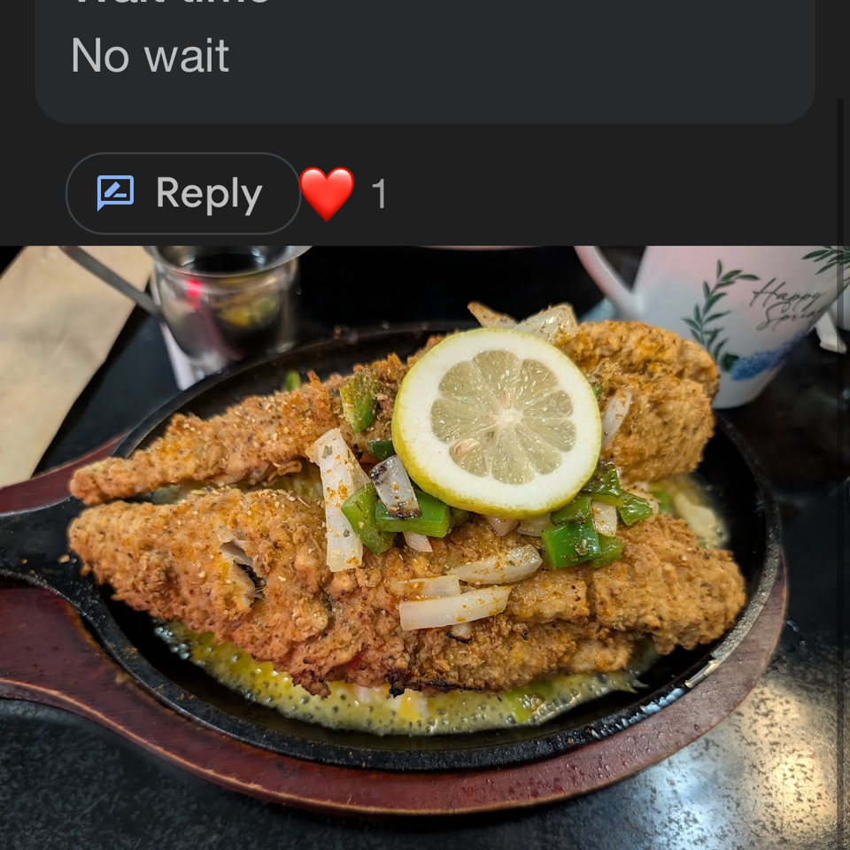 Crispy fried fish fillets topped with sliced lemon, onions, and green peppers in a sizzling skillet.
