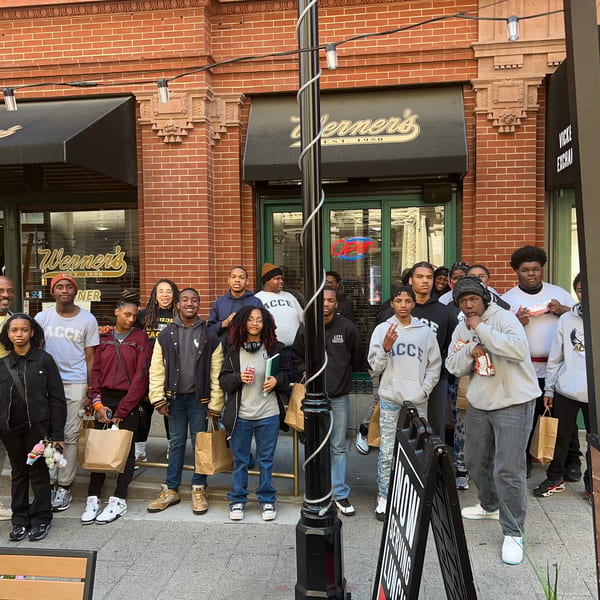 A group of young people and adults stand outside Werner's restaurant, holding brown paper bags.