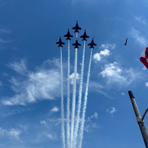 Six Blue Angels jets fly in formation, leaving white contrails against a bright blue sky.