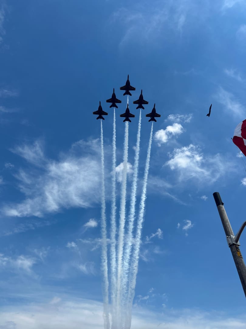 Six Blue Angels jets fly in formation, leaving white contrails against a bright blue sky.