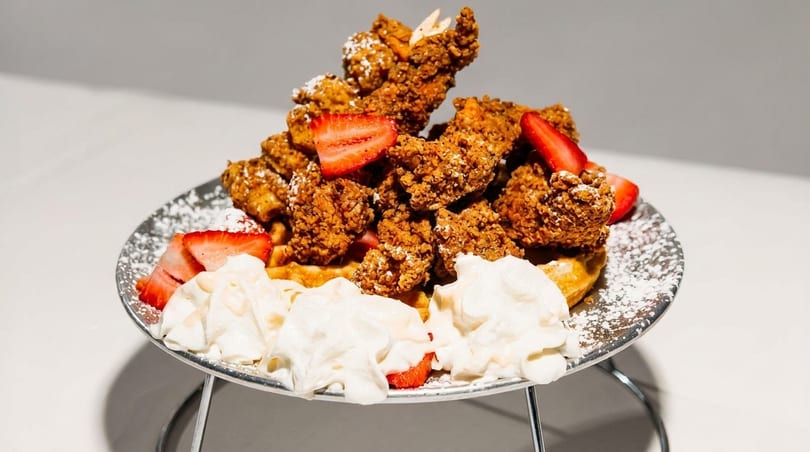 Crispy fried chicken and waffles topped with strawberries, whipped cream, and powdered sugar.
