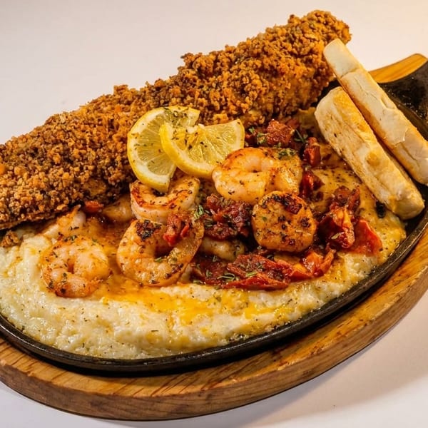 Crispy fried fish, shrimp, and grits with lemon slices and breadsticks in a skillet.